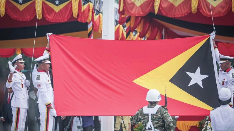 A bandeira nacional de Timor-Leste é hasteada durante um desfile militar que marca o 24º aniversário da Restauração da Independência em Tasitolu, Díli, em 20 de maio de 2026
