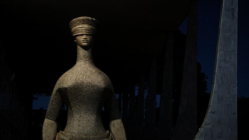 Estátua de pedra da Justiça em frente a um prédio moderno com colunas curvas e fachada branca