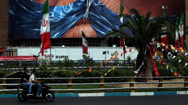 Iranianos passam de carro por um outdoor com a imagem do presidente dos EUA, Donald Trump, e o Estreito de Ormuz, erguido na Praça Valiasr, em Teerã, na quinta-feira, 28.