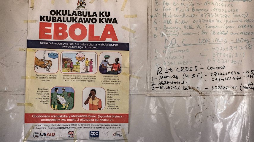 Cartaz com os números de contato de emergência para o Ebola está afixado em uma tenda na passagem de fronteira de Busunga, entre Uganda e a República Democrática do Congo, em Bundibugyo, em 18 de maio de 2026 — Foto: BADRU KATUMBA / AFP