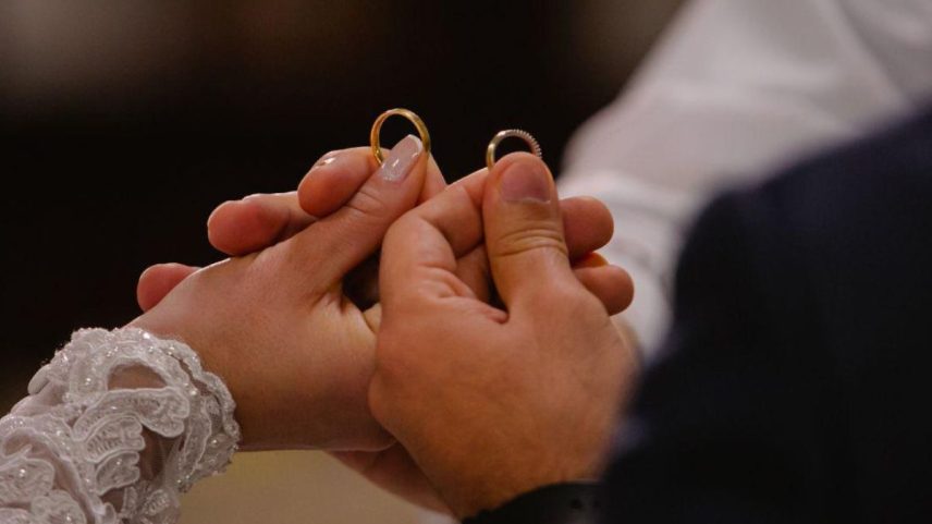 Casal segurando alianças de casamento durante cerimônia