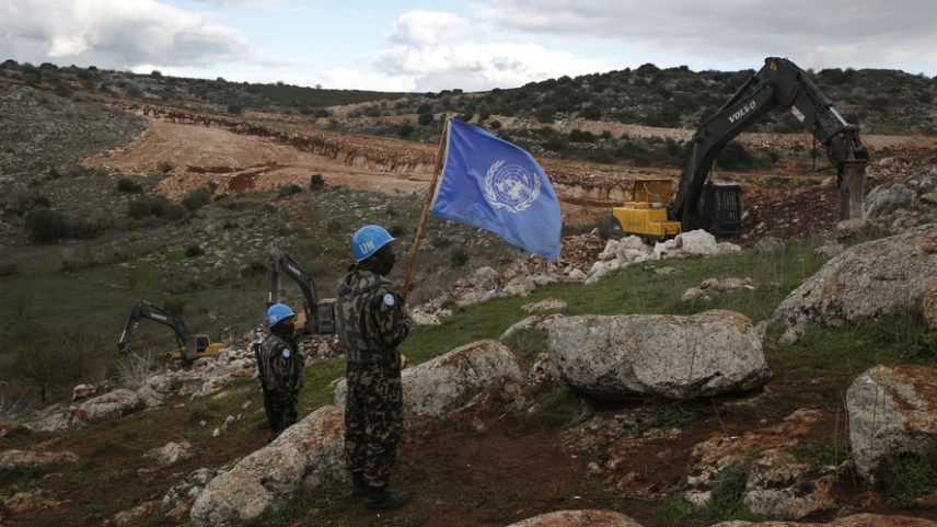 Soldados de paz da ONU seguram sua bandeira enquanto observam escavadeiras israelenses tentando destruir túneis construídos pelo Hezbollah