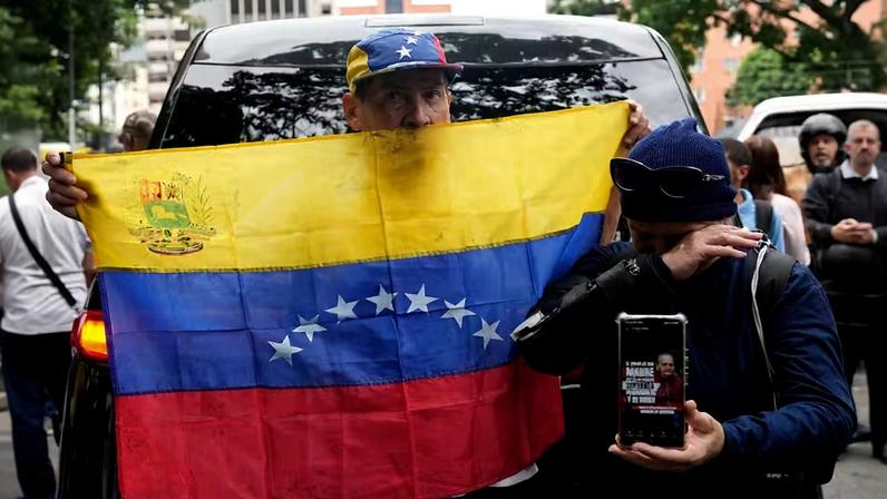 Um homem segura uma bandeira venezuelana em Caracas, Venezuela, na terça-feira, 19 de maio de 2026, durante o velório de Carmen Navas, mãe de Víctor Hugo Quero, que, segundo as autoridades, morreu sob custódia após ter sido detido cerca de um ano antes