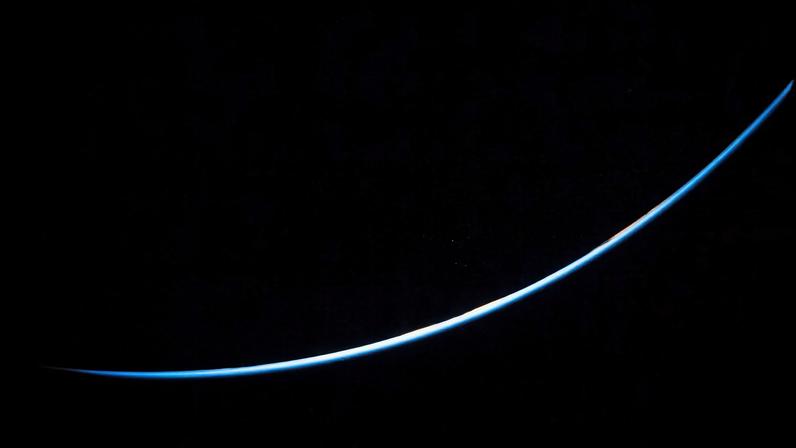 The edge of Earth is a thin line curving upward from left to right. The line is different shades of blue.