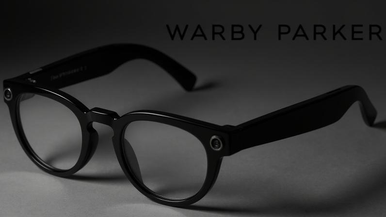 Google An image of Google's new smart glasses. They are slightly rounded frames in a dark green colour with small camera lenses in the corner of the frames on both sides.