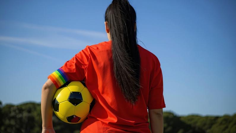 Soccer player woman with a soccer ball and captain armband with the LGBT pride flag on the field. Campaign against homophobia in football. LGBTQ people in sport concept. Women's Football.