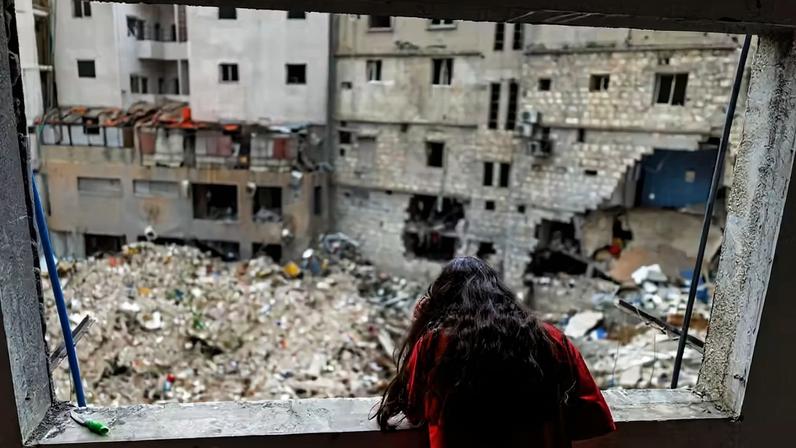 Alaa Dahnoun, de 12 anos, que disse ter sobrevivido a um ataque israelense que a obrigou a fugir com os pais para Beirute, olha pela janela danificada de seu apartamento após a entrada em vigor de um cessar-fogo de 10 dias entre o Líbano e Israel, em Nabatieh, Líbano