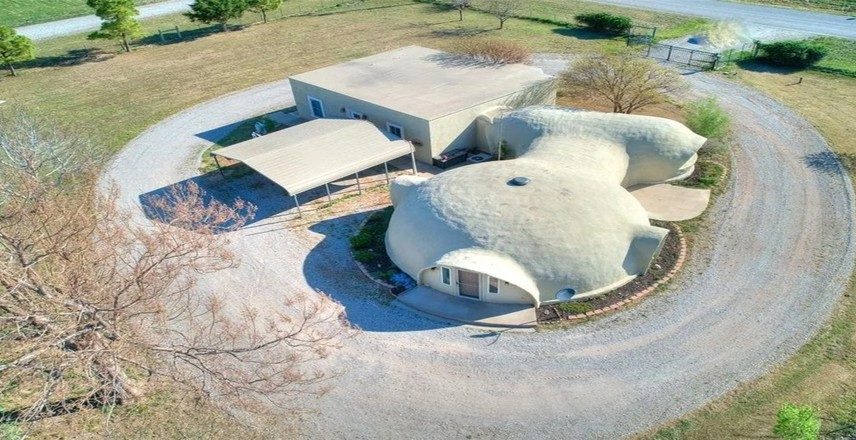 Vista aérea revela a casa em forma de domo integrada ao terreno rural em Oklahoma, EUA. A estrutura curva de concreto foi pensada para resistir a tempestades e tornados