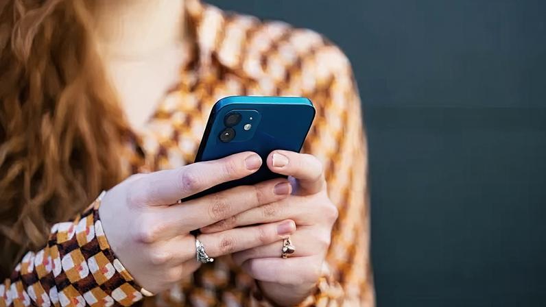 Getty Images A smartphone being read, held in the hands of a woman with long, wavy, red hair and wearing a brown, orange, white and red-patterned shirt.