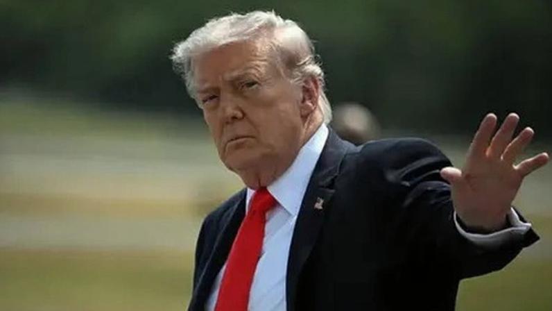 AFP via Getty Images Donald Trump, wearing a suit, raises a hand towards the camera.