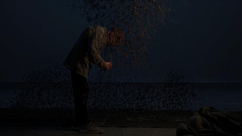 A man crouched beneath a suspended wire sculpture.