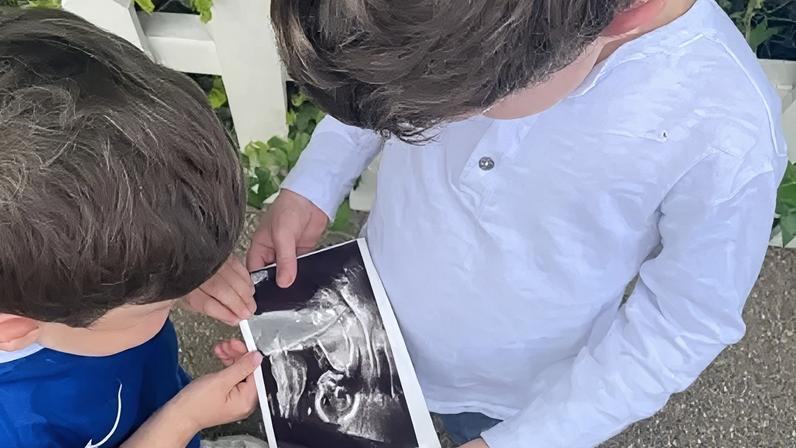 Buckingham Palace Two children look at a picture of a black-and-white baby scan - one boy wears a blue football shirt and the other a pale grey long-sleeved top