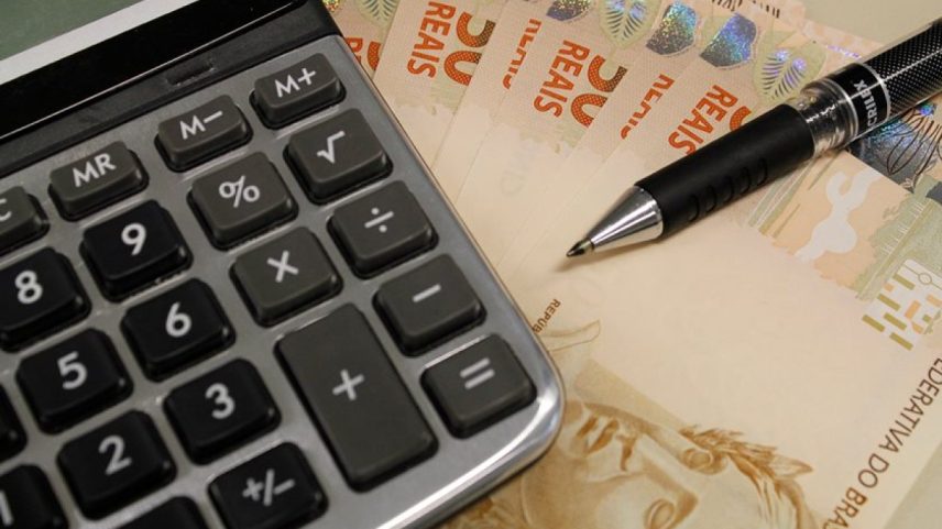 Imagem colorida de uma calculadora e notas de dinheiro - Metrópoles