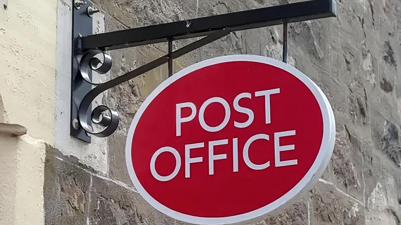 Getty Images A red and white Post Office sign attached to a historic stone wall being held by a black metal beam