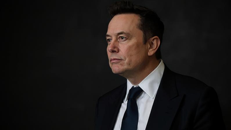 Getty Images Elon Musk wearing a black suit, white shirt, and black tie looking into the distance