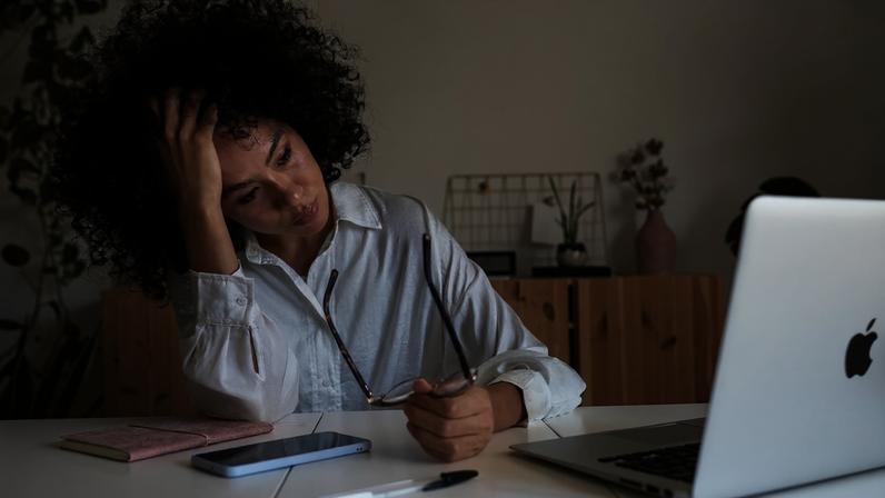 Jovem afro-americana sentindo-se exausta e deprimida sentada em frente ao laptop. Síndrome de burnout no trabalho. Conceito de saúde mental. Metrópoles
