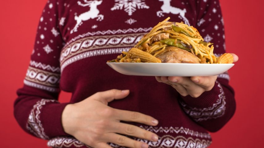 Foto colorida com fundo vermelho e uma mulher segurando um prato enorme de comida - Metrópoles.
