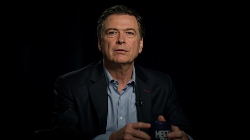 NBC via Getty Images James Comey wears a suit and holds a mug on the set of NBC News' Meet the Press.