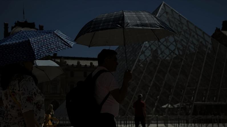 Visitantes usam guarda-chuvas para se proteger do sol durante as altas temperaturas no Museu do Louvre, em Paris, França, em 26 de maio de 2026.
