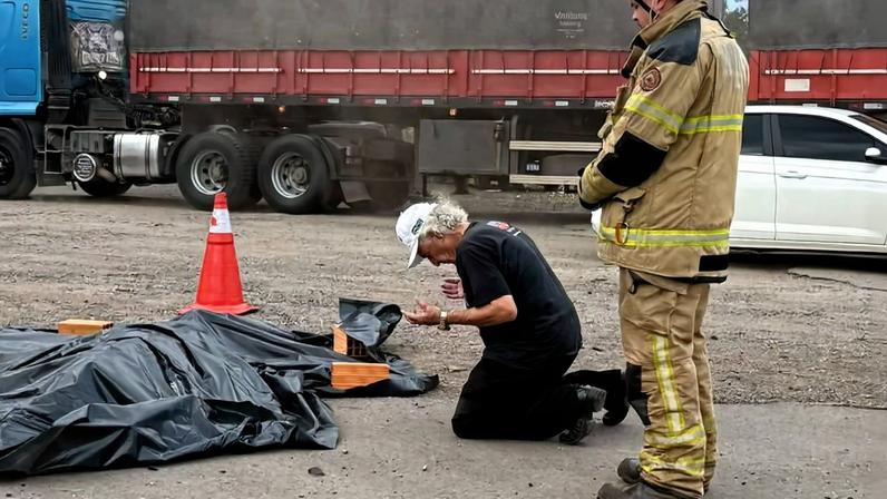 Imagem colorida, Após acidente, homem ajoelha e ora ao lado de motociclista morto no RS- Metrópoles