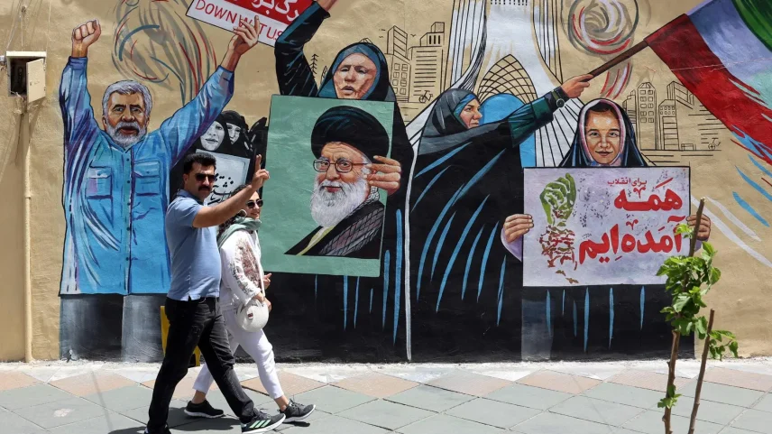 Casal iraniano caminha em frente a mural que critica Estados Unidos e Israel em Teerã, capital do país (Foto: EFE/EPA/ABEDIN TAHERKENAREH)