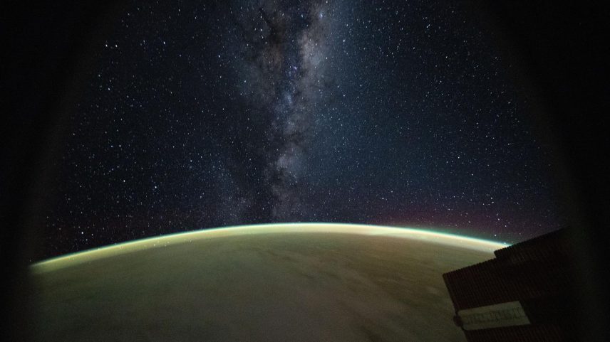 This celestial image captured from a window on a SpaceX Dragon spacecraft docked to the International Space Station highlights the Milky Way rising above Earth's atmospheric glow.