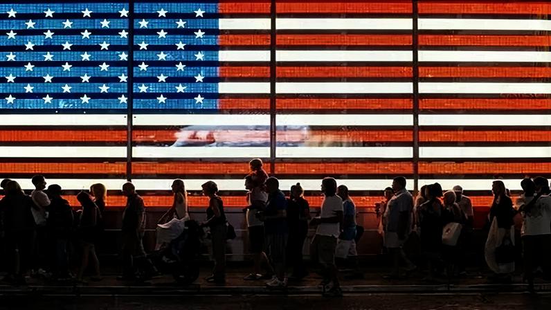Pessoas andam em frente à bandeira dos EUA