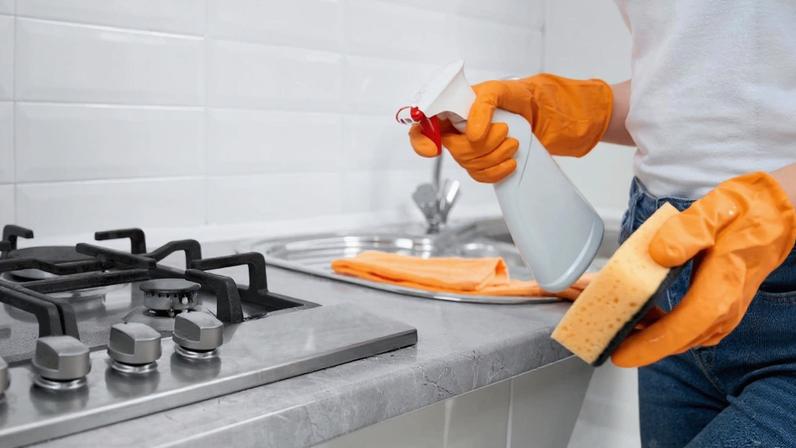 Mão segurando esponja e produto de limpeza em frente a um fogão