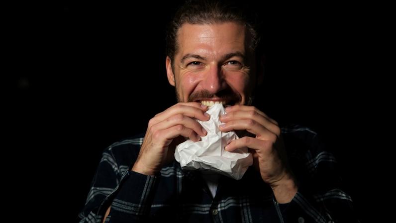 Foto colorida de um homem comendo papel - Metrópoles