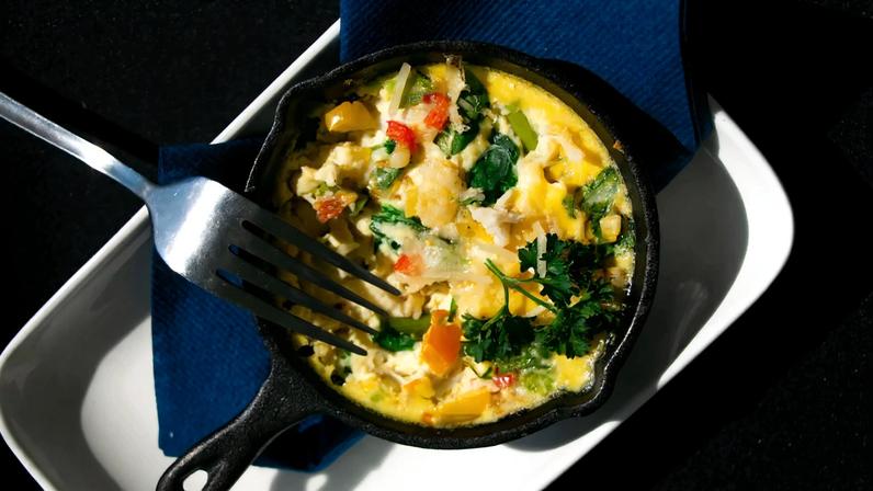 A small cast iron of savory eggs and vegetables sits on a serving plate after being tasted.