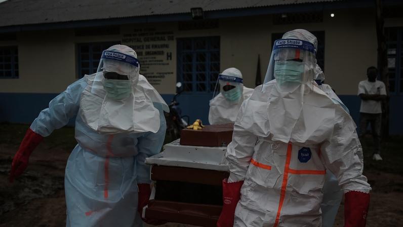 Equipe médica usando equipamentos de proteção individual (EPI) carrega o corpo de um paciente falecido no hospital de Rwampara nesta quinta (21/05)