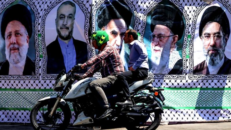 Homem passa de moto em frente a imagem do falecido líder supremo iraniano, o aiatolá Ruhollah Khomeini (C), o líder supremo assassinado Ali Khamenei (2º à direita) e seu filho, o atual líder Mojtaba Khamenei (à direita). Crédito: ATTA KENARE / AFP