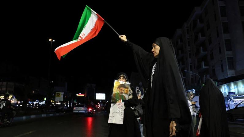Mulheres seguram a bandeira nacional do Irã e uma foto do líder supremo do país, o aiatolá Mojtaba Khamenei, durante um protesto contra os EUA e Israel, em Teerã.