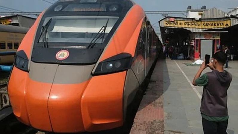 An orange Vande Bharat Express sleeper train stands at a station platform as a boy takes a photo of it (Credit: Jamie Fullerton)