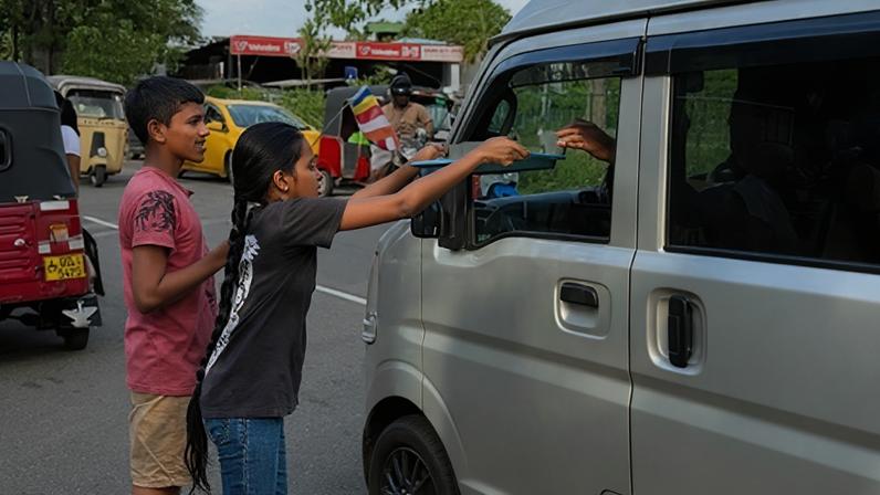 Zinara Rathnayake A young girl offers a tray of drinks through the window of a white van on a busy Colombo street during Vesak (Credit: Zinara Rathnayake)
