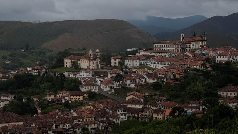 Centro histórico de cidade mineira com igreja e morros ao fundo