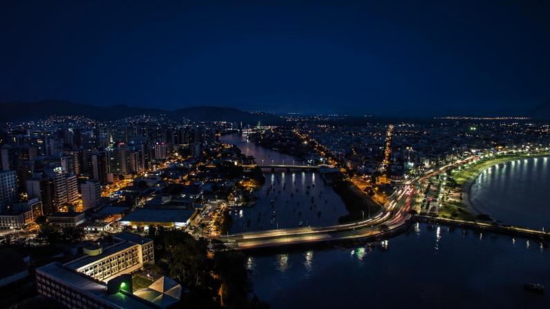 Vista aérea de Vitória ES ao pôr do sol, com a Terceira Ponte e a baía ao fundo.