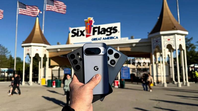 A man is holding the Samsung Galaxy S26 Ultra, the Pixel 10 Pro, and the Motorola Razr Fold in front of an amusement park while conducting some long-distance photo shooting.