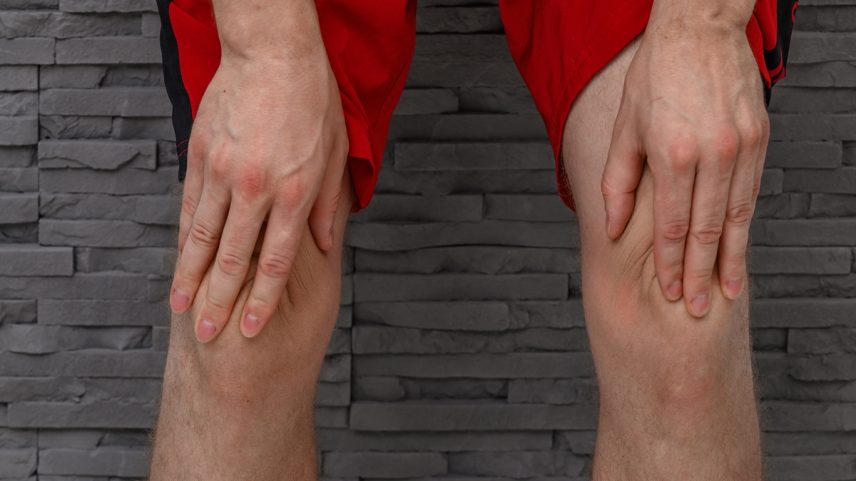 Foto colorida de pernas masculinas com mãos diretamente no joelho simulando dor causade pela sarcopenia - Metrópoles.