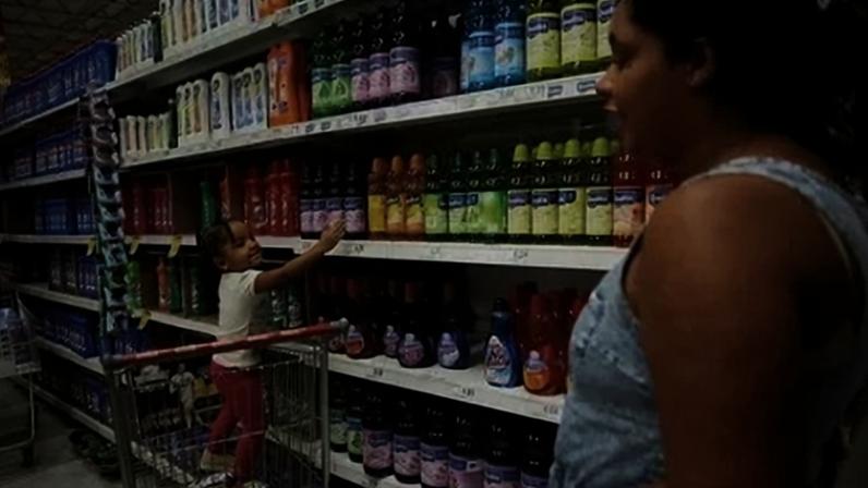 Criança está em um carrinho de compras enquanto aponta produtos de limpeza ao lado de sua mãe em um supermercado em São Paulo, Brasil