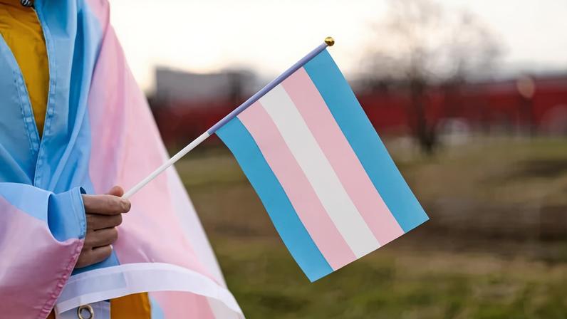 Transgender covered with the transgender flag and holding a flag in the hand for defending her rights