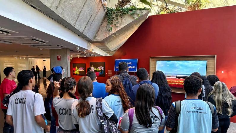 Foto colorida mostra estudantes na exposição