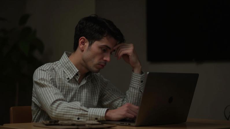 Homem com camisa xadrez, rosto e mão em tom magenta, trabalha no notebook com expressão de cansaço. Ao fundo, imagens em verde e magenta de alimentos processados: embalagem plástica, biscoitos, molhos e uma mão pegando salgadinho de um pote