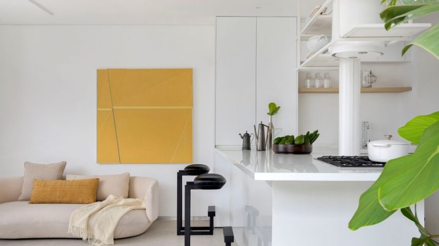 LIVING INTEGRADO | Na sala de estar, sofá Baixo, assinado por Guilherme Wentz. Bancada da cozinha feita de Nanoglass. As banquetas de bar Gávea, de Jorge Zalszupin, na Etel Interiores, e o quadro do artista Mateus Machado quebram a monotonia dos tons claros. Almofadas e manta da Branco.casa