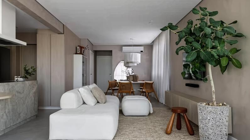 LIVING | A paleta neutra cria uma atmosfera calma no espaço com ambientes integrados, como desejavam os moradores. Texturas, como o tapete de tear manual, da Nomad Casa em Movimento, e a parede pintada com Velvet, da Suvinil, além da marcenaria clara, como rack executado com MDF, no padrão carvalho americano, da Greenplac, pela Móveis Zonta, completam o visual aconchegante. Banco da Tempo Casa. Planta figueira-de-bengala confere um toque de cor