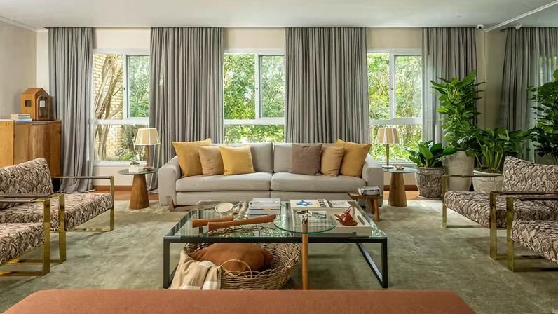 SALA DE ESTAR | Sofás e poltronas receberam novos revestimentos, transformando a atmosfera do ambiente sem a necessidade de substituir as peças. O cesto de cipó da Divinos Trancoso fica abaixo da mesa de centro da Vermeil, loja que também forneceu o banco e o oratório. Mesas laterais da Allez Decor, com abajures da Entreposto, loja onde as almofadas também foram adquiridas. Tapete da Botteh. Ao fundo, ⁠paisagismo de Chris Pierro, com espécies jiboia (vaso mais alto), pacová (à esquerda) e costela-de-adão (ao lado do espelho).