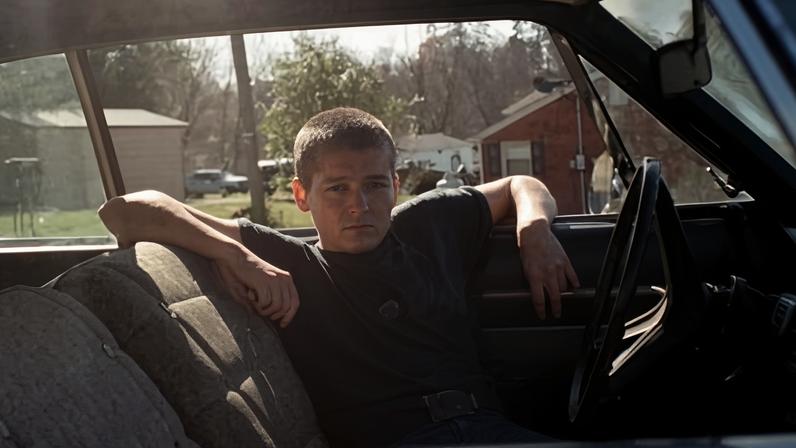 Zoh Amba, musician, pictured in a car with elbow resting on open window in the sun
