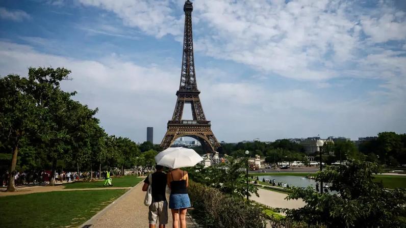 Pessoas se protegem do sol com um guarda-chuva perto da Torre Eiffel, enquanto as temperaturas sobem em Paris durante a segunda onda de calor que afeta grande parte da França. Em 20 de junho de 2026.