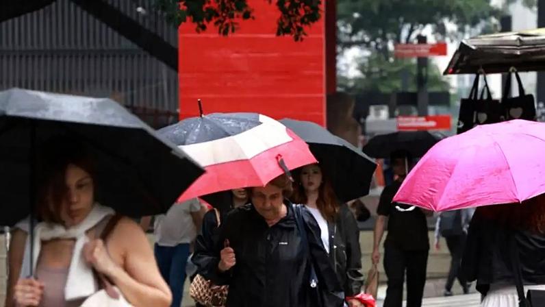Pedestres caminham com guarda-chuva