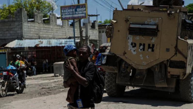 Um homem carrega uma criança enquanto moradores fogem de um bairro após confrontos entre gangues na noite anterior, em Porto Príncipe, Haiti, em 20 de abril de 2026.